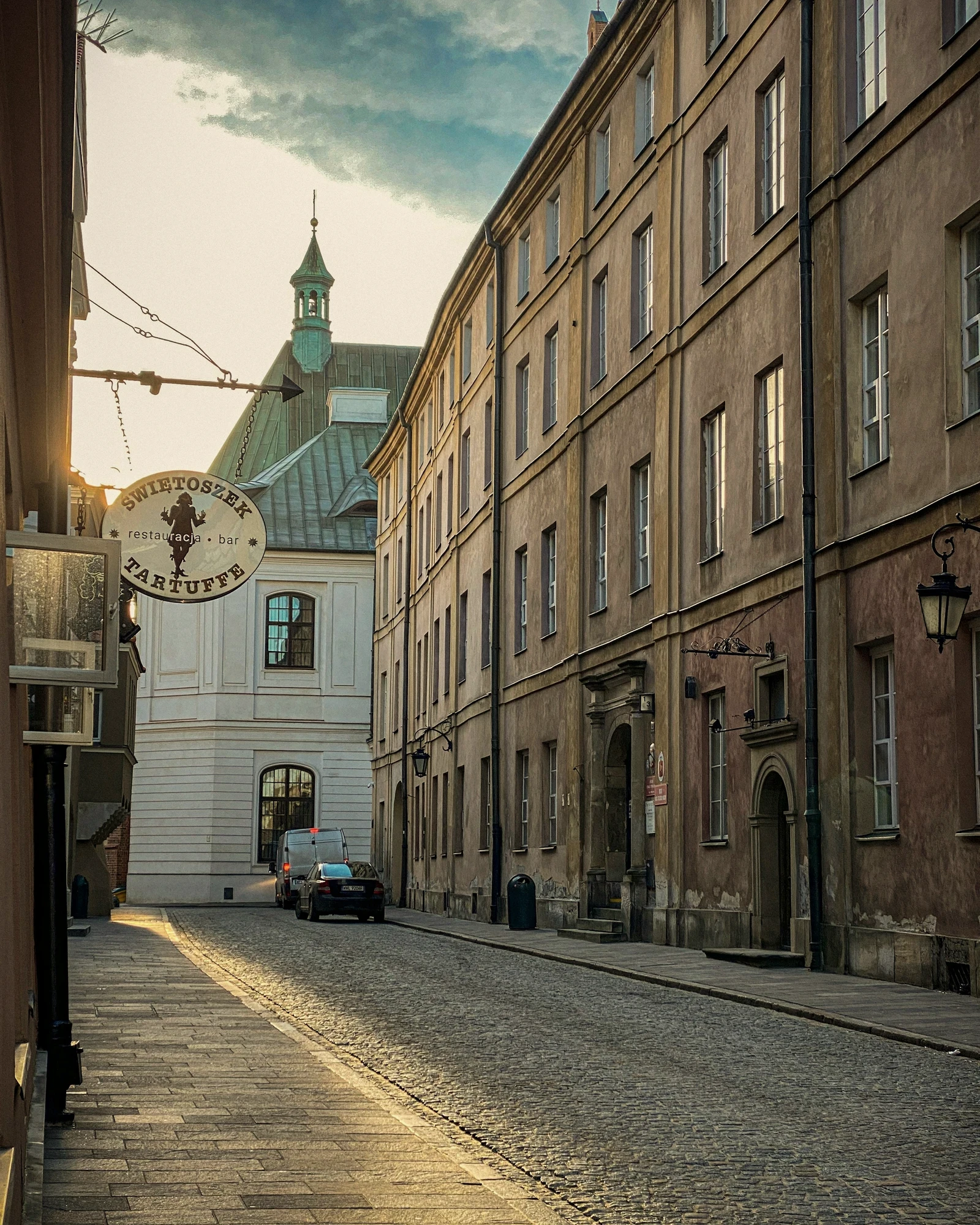 A cobblestone old-town street with a clock tower in evening light