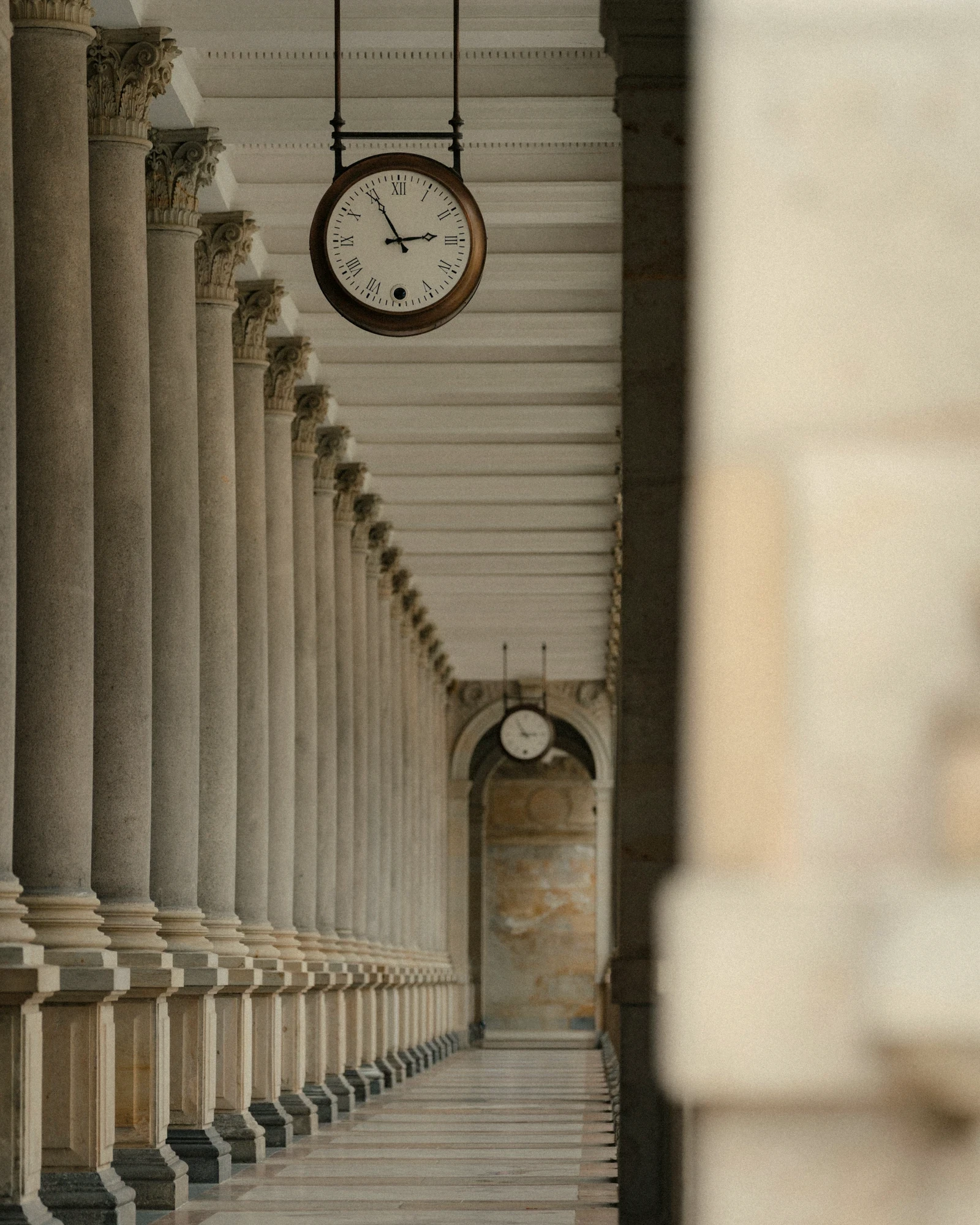 A stone colonnade with an old clock hanging from the ceiling