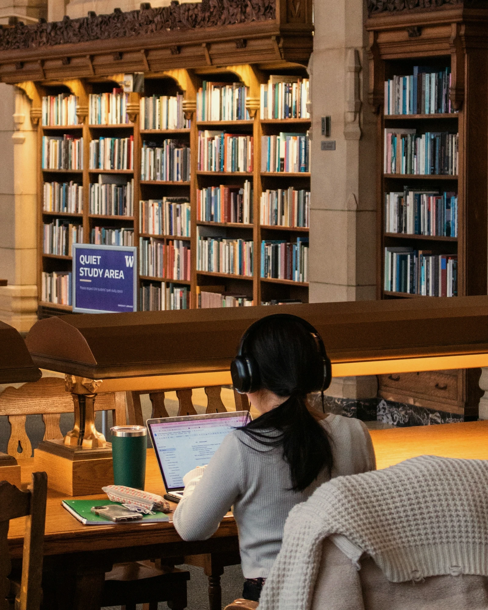 A student working on a laptop in a warm, quiet library